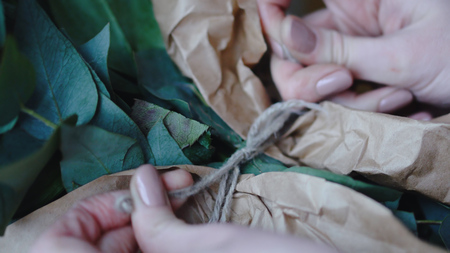 Female florist makes a bow from a thread on a bouquet for sale in a flower shop. Close upの写真素材