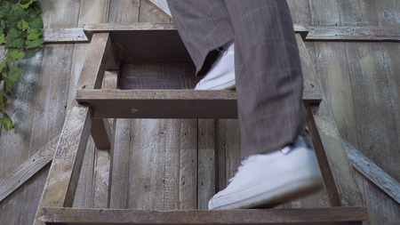 A girl in trousers and sneakers rises to a wooden stepladder: legs close-up photo