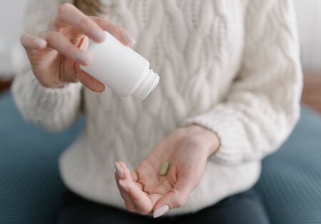 Last antibiotic tablet - a woman pours the last medicine from the package into the palm of her hand. Treatment with expensive drugs. The concept of medicine and pharmacyの写真素材