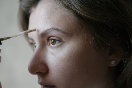Woman puts a beige tone on her skin. Preparation, application of makeup. Close-up portrait