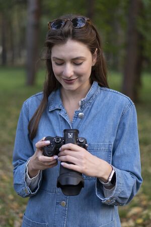 Black camera in female hands. A woman in denim clothes looks at and chooses the footage on a mirrorless camera in the streetの写真素材