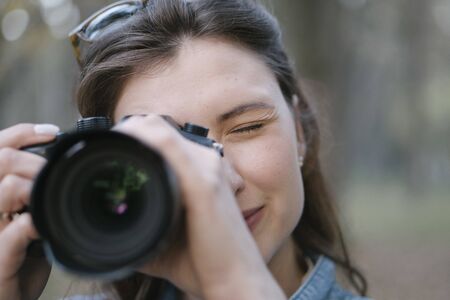 A girl with brown hair takes a picture on a mirrorless camera. A portrait of a photographer with a...