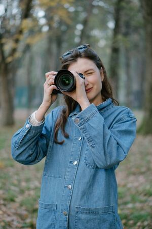 Portrait of a professional freelancer with a camera in hand in the autumn forest at sunset. The girl smiles and looks into the cameraの写真素材