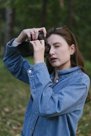 A young female photographer in nature, shoots wildlife in the fall in the woods. Hobby or profession photographyの写真素材