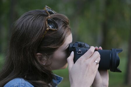 A beautiful girl takes a picture on a dslr camera, close-up. Blogger creates content outdoors