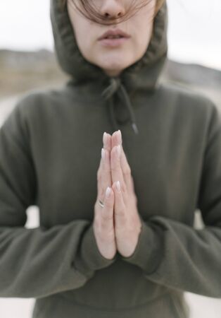Yoga outdoors, a young calm woman meditates in a green hoodie. Close-upの写真素材