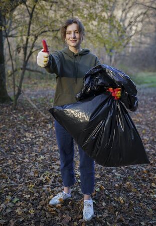 Portrait of a beautiful volunteer woman with a garbage bag in her hands. Holding a campaign to clean up the forest from debris. The girl smiles and shows likeの写真素材