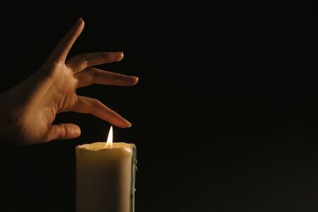 Esoterics and magic - women's hand conjure over a lit candle on a black background. Paronormal Activity and Clairvoyance by Deception.の写真素材