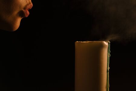 Spiritual session - a woman blows out a burning candle. Isolated, black background. The concept of religion, faith, magic and witchcraft.の写真素材