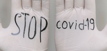 Black inscription on white medical gloves STOP covid-19. Health and medicine during the coronavirus pandemic. Close-up bannerの写真素材