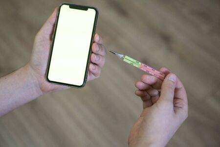 The man is holding a medical thermometer and a phone, on the screen of a chromakey. The concept of...