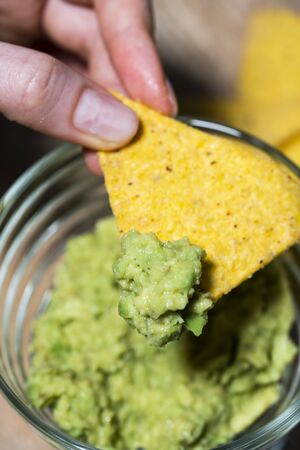 Person scoops up nachos chips with fresh Mexican guacamole sauce. Snack for the party, close-upの写真素材