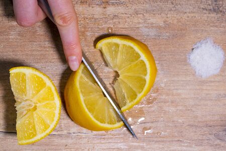 Female hand cuts into slices fresh lemon on a wooden table. Salt for tequila in the background. Guacamole recipe, top viewの写真素材