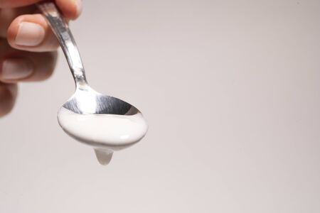 Spoon with eco yogurt in a woman's hand on a light background, close-up.の写真素材