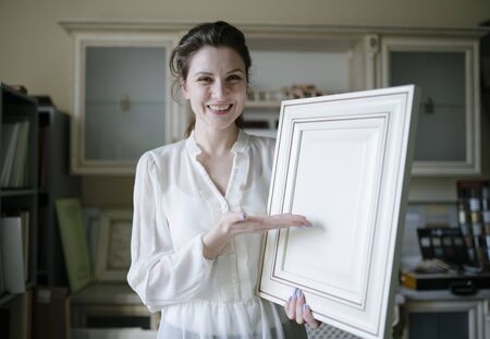 A female seller demonstrates an example of furniture for the kitchen. A young small business owner looks at the camera and smiles in a furniture storeの写真素材