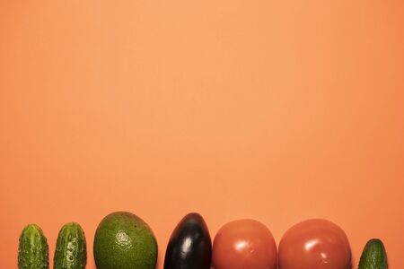 Group of vegetables on a peach background, eggplant in the center. Fresh vegan products close up. Diet for a healthy lifestyle, flat lay copy spaceの写真素材