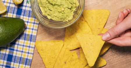 Person eats guacamole with nachos chips at a party, close-up. Delicious snack for the company, vegetarian foodの写真素材