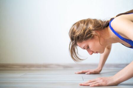 A young woman doing push-ups in her apartment. Slender and sporty girl is engaged in sports at home....