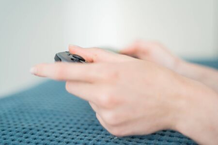 The girl plays on handheld console lying on the blue bed. Game controller in female hands close-up. A portable game consoleの写真素材