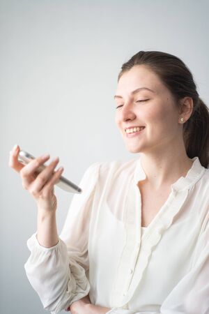 A happy woman communicates with a voice assistant on her phone. Reaction to a personal assistants responseの写真素材