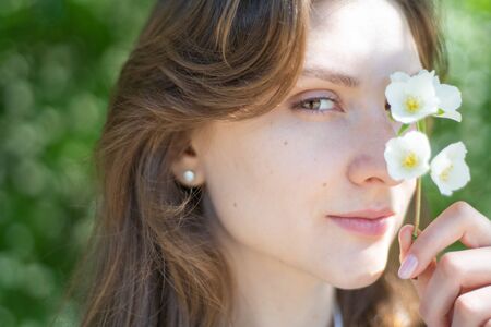Portrait of a young woman close-up, covering her eye with a branch of jasmine. Beautiful smiling girl with flower in her handの写真素材