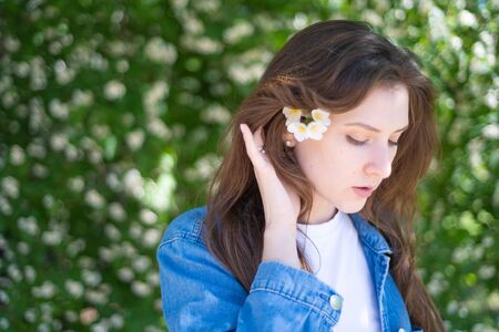 Millennial girl with flower. Woman in a denim jacket enjoys life and holds in her hand a beautiful white jasmine flower, copyspaceの写真素材