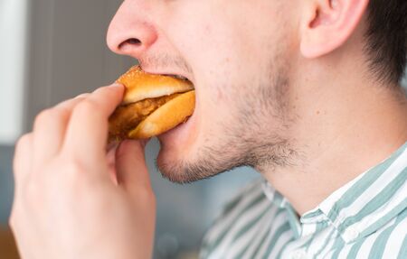 A man eats junk food, a close-up. Guy bites chicken burger.の写真素材