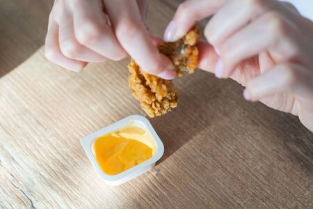 Nuggets are broken and dipped in sauce. Chicken fast food, fried wing in breadcrumbs in female handsの写真素材