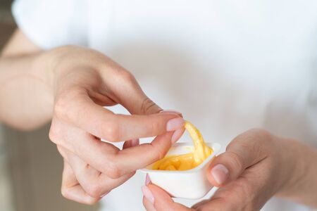 French fries dip in sauce. Fast food in womens hands close-up. Obesity and unhealthyの写真素材