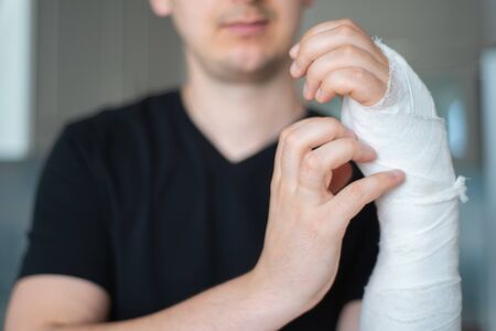 Itching under bandage. Man tries to scratch broken arm, close-upの写真素材