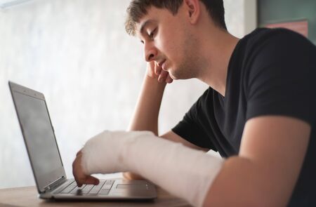 A man with an arm injury looks into a laptop. Online diagnosis. Health insuranceの写真素材