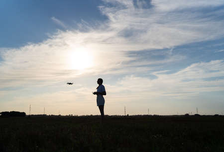A professional drone pilot controls it against the sunset sky. Copter operator silhouetteの写真素材