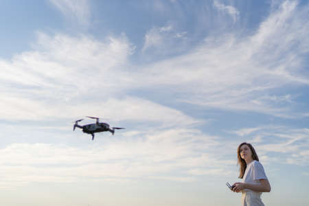 A woman controls the flight of a drone. The quadcopter hovered in the air, the female drone pilot looks at the droneの写真素材