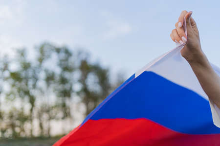 The flag of Russia in womens hands against the backdrop of a beautiful sunset and treesの写真素材