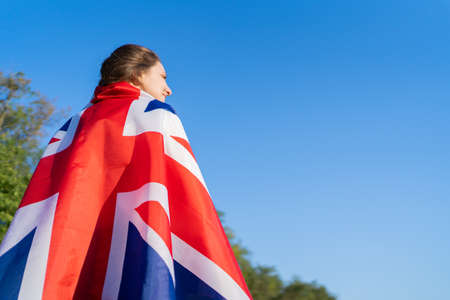 A British woman stands with the national flag on her back and looks into the distance. British...