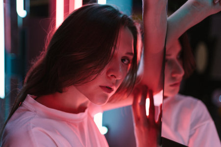 The colored bright pink lighting on the face of a beautiful young woman is close-up. Portrait in a...