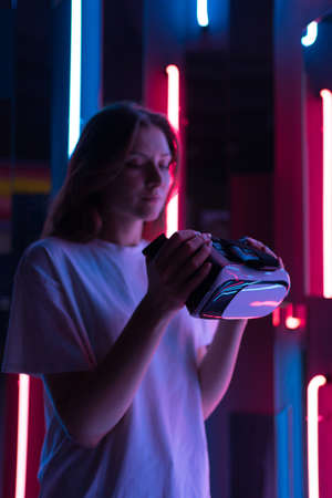 Beautiful young woman putting a VR headset against the background of multi-colored neon lamps