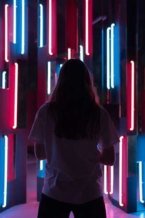 Vertical shot - a view from behind on the silhouette of a woman standing in neon lightの写真素材