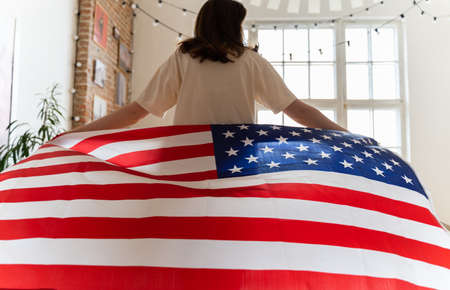 The American flag beautifully waving behind a woman walking into the light. July 4 in the USA