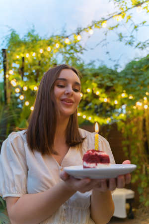 Birthday party. A young woman with cake and one candle in illuminated patio. Happy Holidayの写真素材