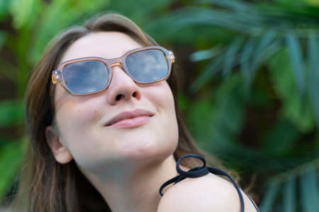 Pretty young woman in sunglasses looks at the sunset. Summer in the jungle. Happy person, close-up portraitの写真素材