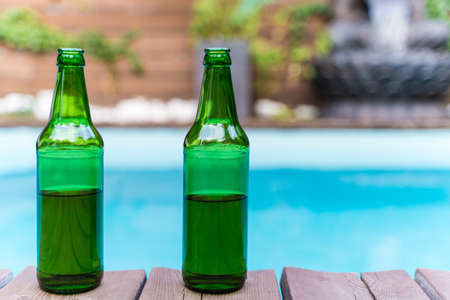 Two green bottles of beer without a logo outside. Swimming pool in the tropics. Alcohol at a patio party. No peopleの写真素材