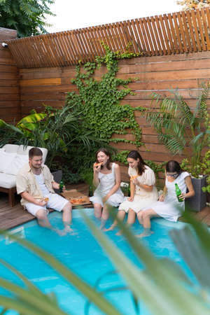 Celebration in the pool. Friendship of a group of people. Toast, beer bottles, cheer. Pizza time