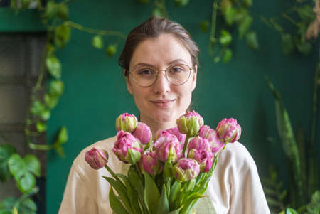 Portrait of a young adult entrepreneur. Professional florist with a bouquet of pink peony tulips....