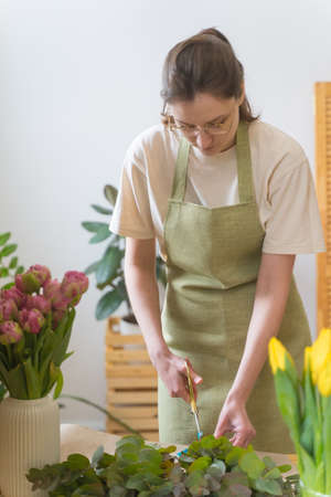 Small business. The owner of a flower shop in a green apron collects a bouquet of fresh flowers for...