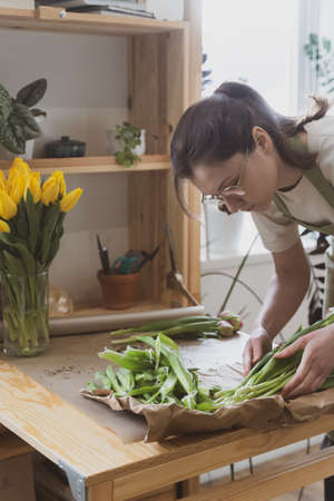 A woman florist in glasses and an apron works behind the counter in a flower shopの写真素材