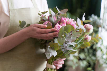 Professional florist checks a beautiful bouquet before sending it to the customer. Fresh flowers in the hands of a young woman close-up. The concept of small business and women entrepreneursの写真素材