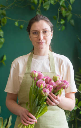Successful young woman - small business owner. Professional florist with a beautiful bouquet of fresh flowers in the store looks into the cameraの写真素材