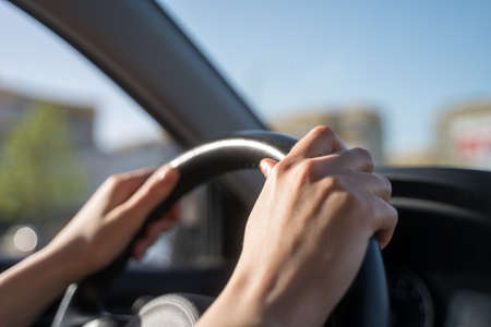 Hands of the female driver on the steering wheel of the car. Traffic control in motion, close-upの写真素材