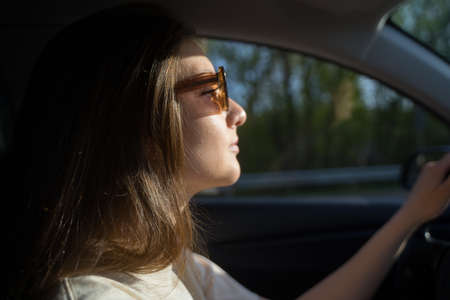 Confident woman drives car in a traffic jam. Businesswoman in sunglasses holds on to the wheel of a...